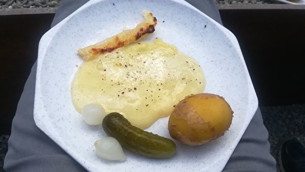 白い皿にとろけたチーズとガーキンとゆでた皮つきじゃがいもがのっている。