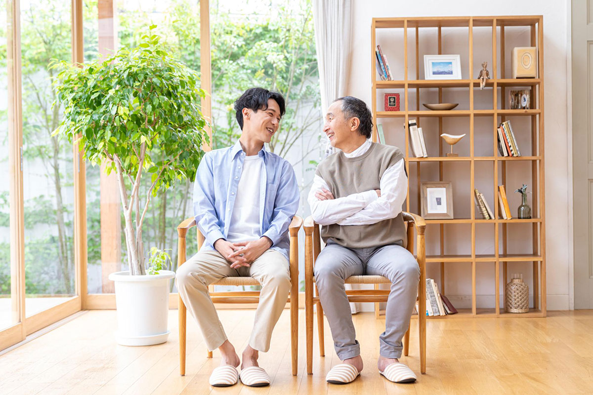 実家のリビングで父親と息子が座って笑顔で語らう様子