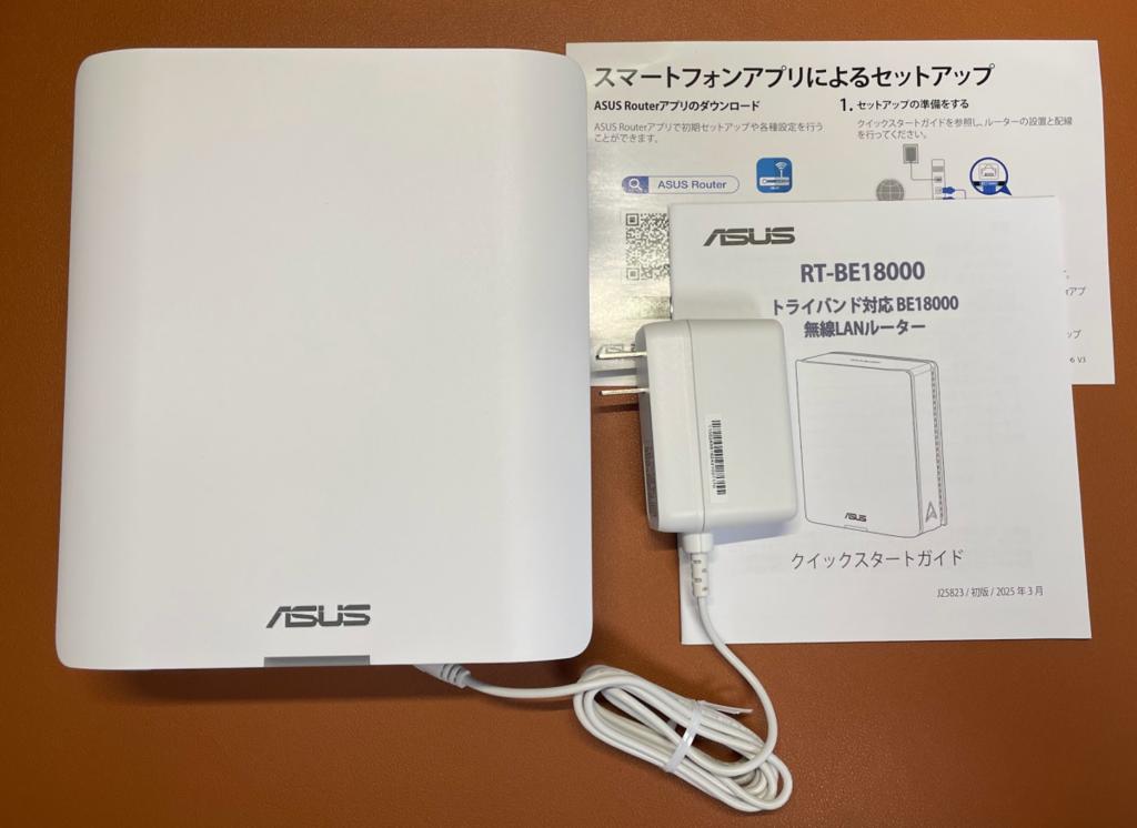 白いルーター本体、白い電源アダプタ、ケーブル、説明書一式が並べられている様子
