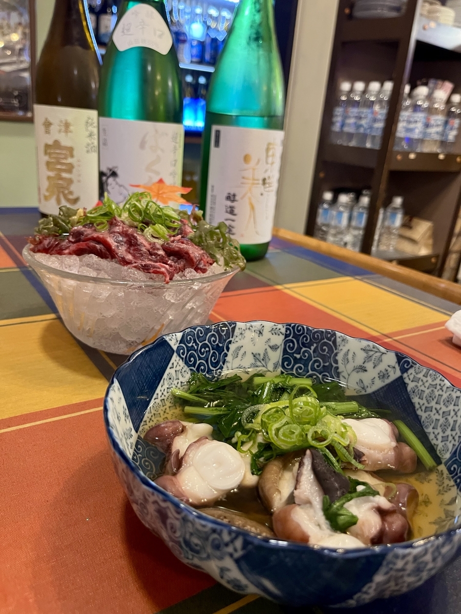 手前にたこの酢の物、その奥に氷の上に載った馬刺し、一番奥に日本酒の一升瓶が3本