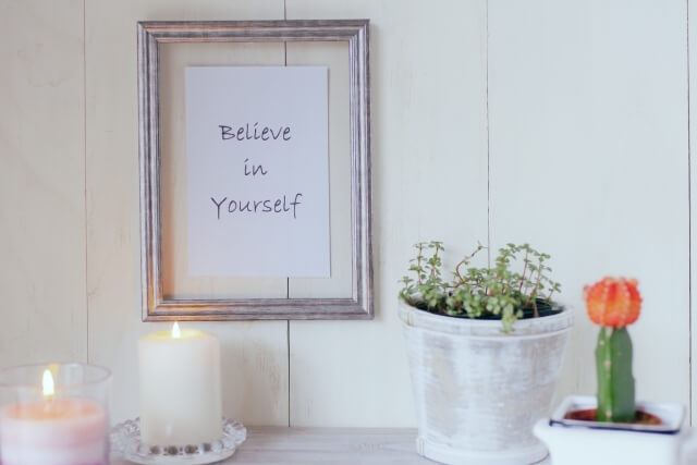 白い壁に「Believe in Yourself」と書かれている額縁が飾られ,ろうそくの灯が2つ点いている。