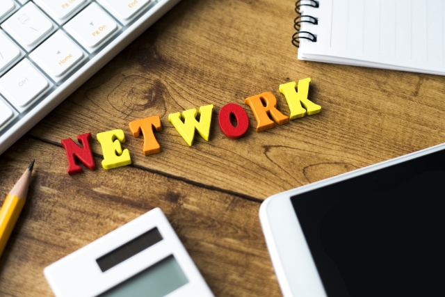 木目の机上に置かれたキーボード,鉛筆,電卓,パッド,メモ帳にカラフルな「NETWORK」の文字
