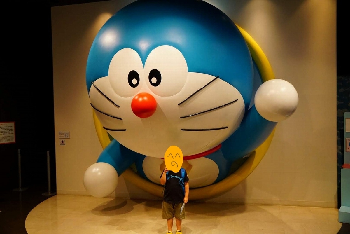 大きいドラえもんの下でピースする子供