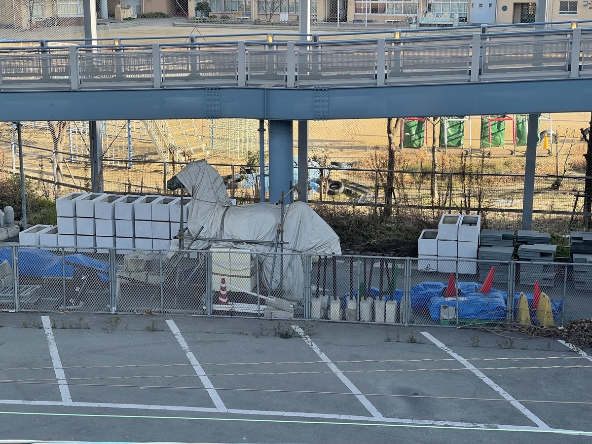 遊歩道から撮った資材置き場。馬のモニュメントのようなものにカバーが被せてある。