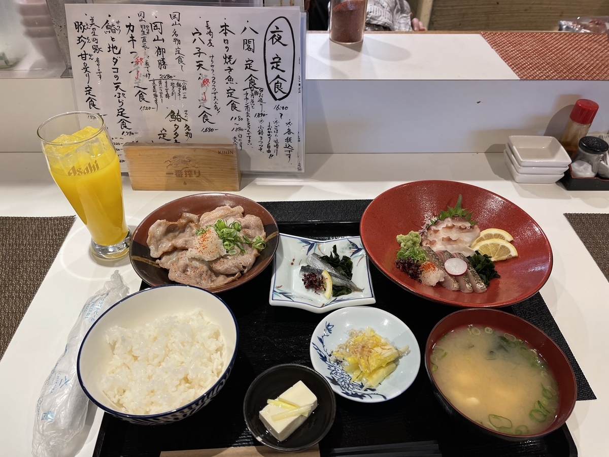 お盆の左手前から右手前にご飯、お豆腐の小鉢、黄ニラのおひたし、お味噌汁が並んでいます。左奥から右奥に美星町の豚の炙り、ままかりの酢漬け、鰆のタタキと地ダコの刺身が入った器が並んでいます。