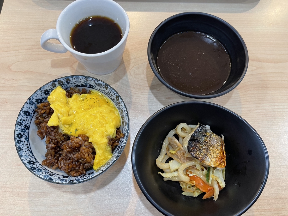 左手前にスクランブルエッグを掛けたえびめし、右手前に焼きうどんと焼き魚、左奥にコーヒー、右奥にカレーを並べています。