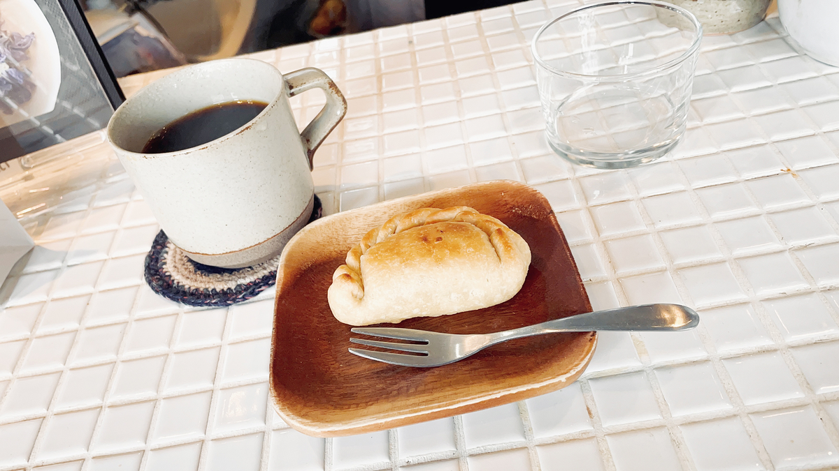 カップに入ったコーヒーと、木のお皿に置かれた揚げ餃子のようなパイ。