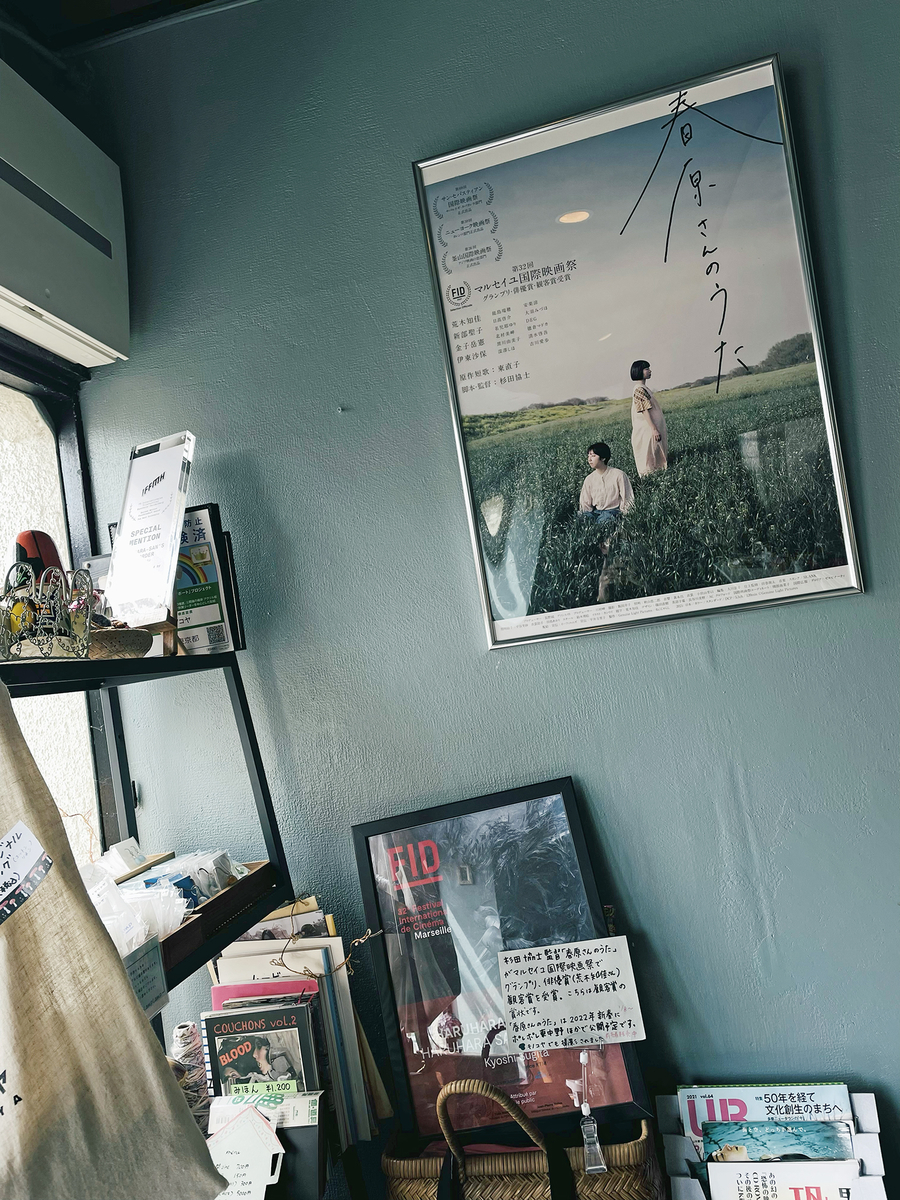 店の隅。淡い青緑の壁に映画のポスターや映画祭のトロフィーなどが雑然と置かれる。