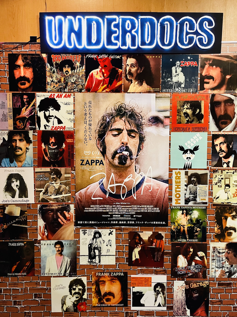 レンガ模様の壁。ポスターの周りに無数のジャケットが貼り付けられている。