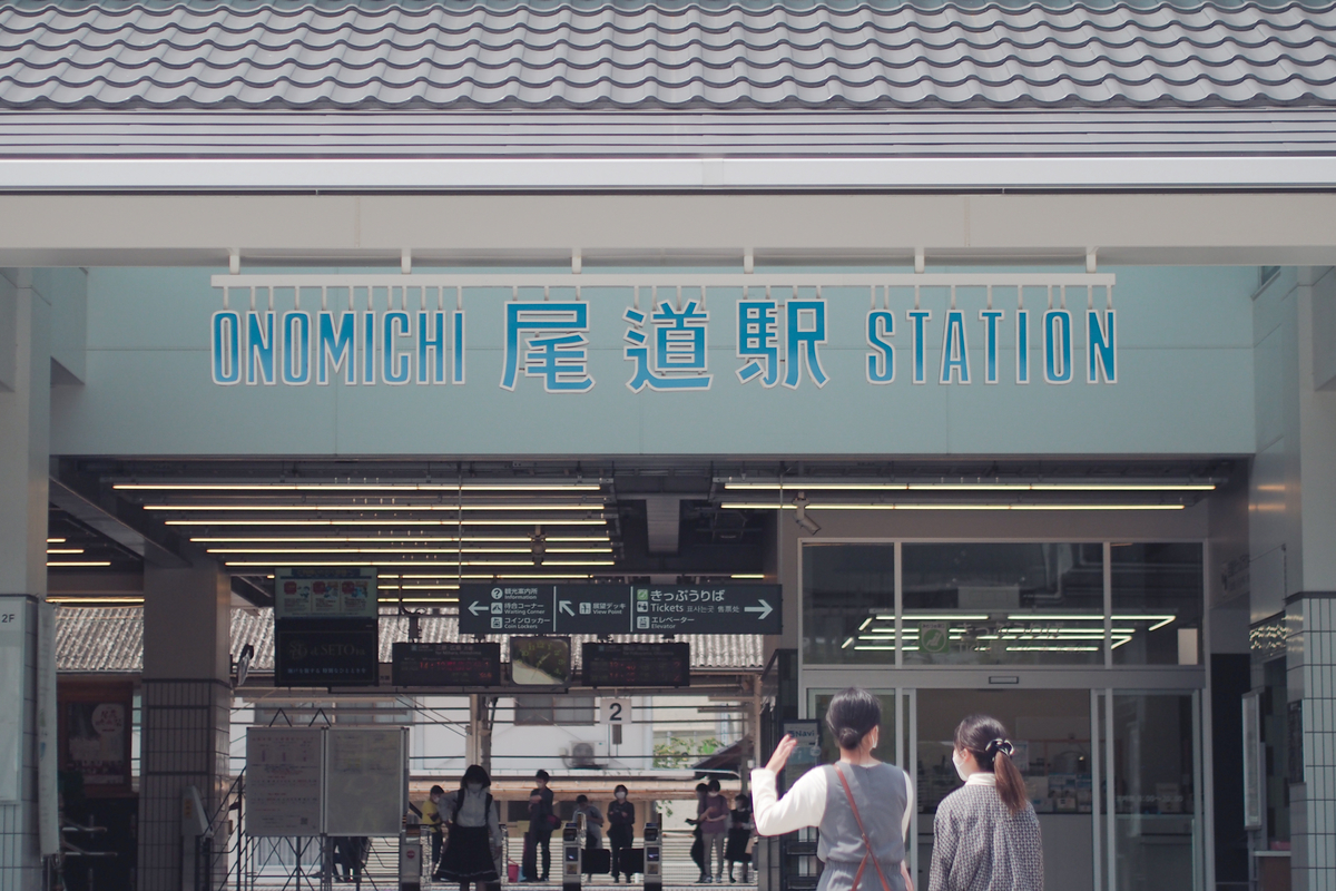 尾道駅、改札口のポップな駅名看板。青色の文字。