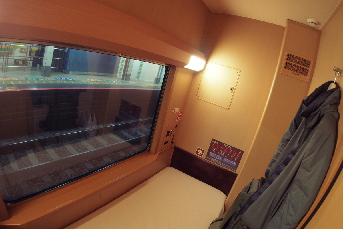 部屋の内部。診療所のベッドくらいの細い寝台と、かなり大きな窓、壁には洋服掛け、寝台の脇にはバッグなどを置けるスペースがある。