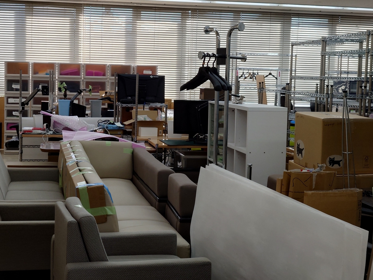 広い部屋の中にたくさんの荷物があり画像手前にはいくつものソファが並べられている．