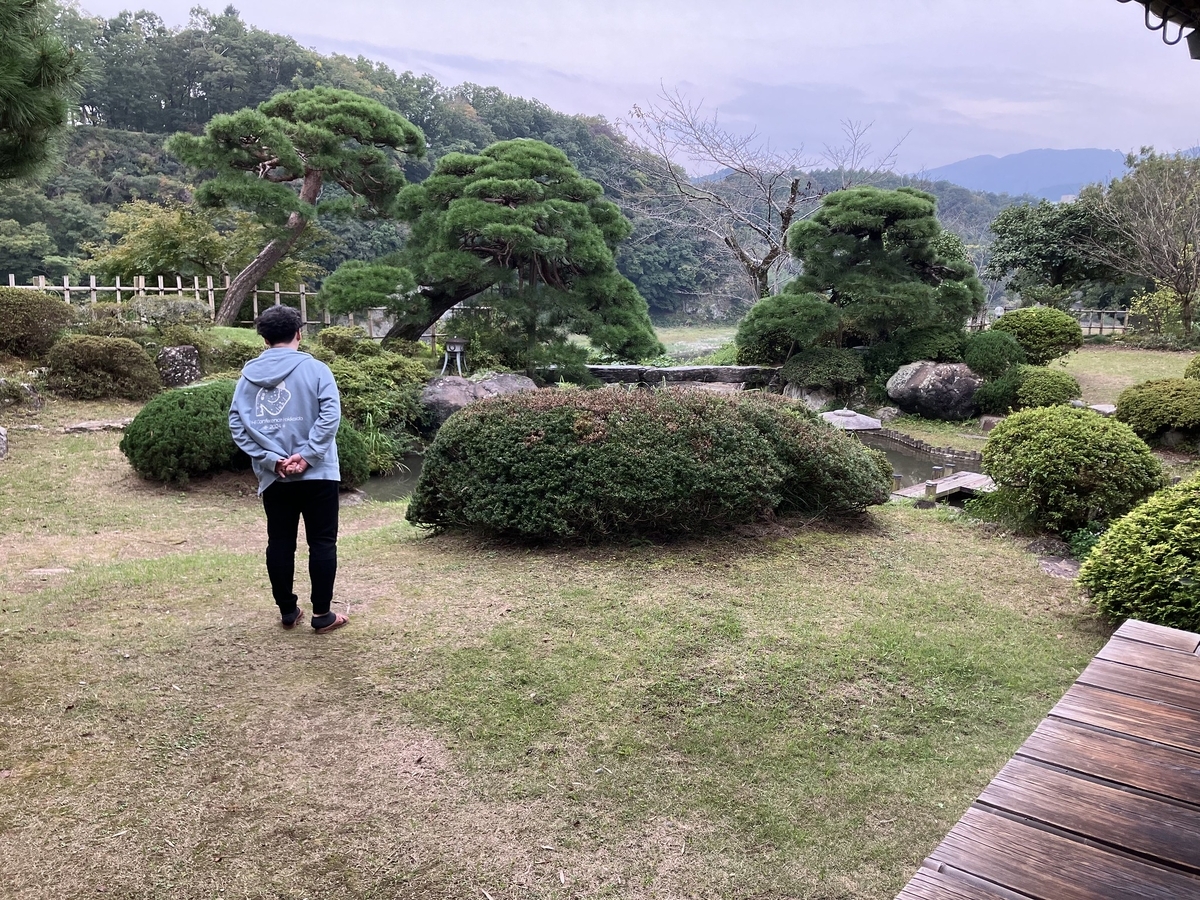 京亭の庭に水色のパーカーをきたさたけさんが佇んでいる様子