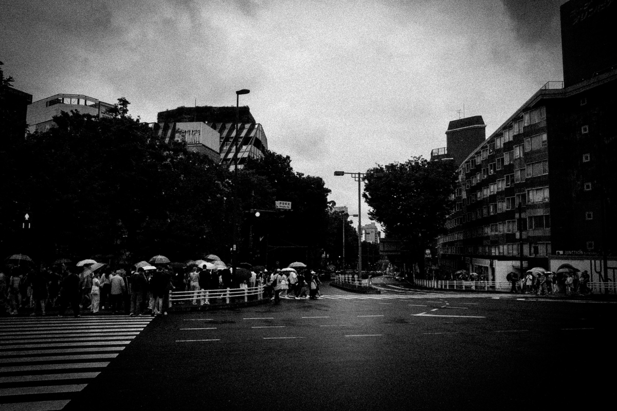 雨の交差点を傘を差して歩く人々