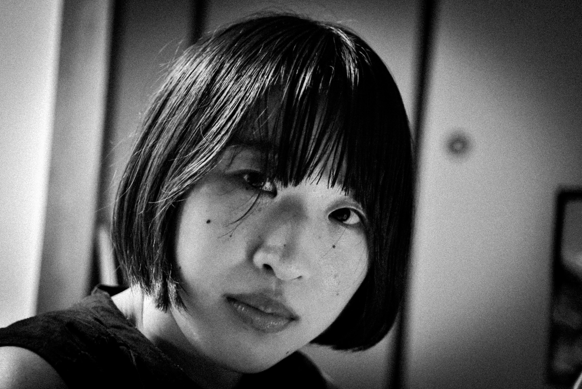 室内でこちらを見つめるボブヘアの女性の顔