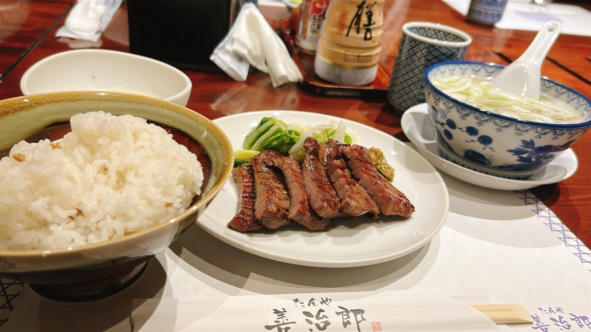 牛タン定食の写真。左にご飯がたっぷりつがれたお茶碗。右奥にはネギがたくさん入った牛テールスープ。そして真ん中には厚みのある牛タンが美味しそうな焼き色で鎮座している。