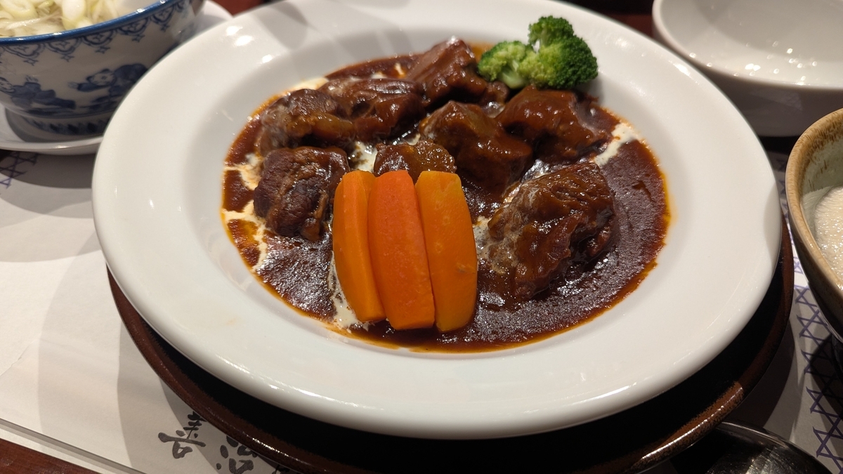 白いお皿に牛タンのビーフシチューがたっぷり入っている。にんじんのオレンジとブロッコリーの緑がアクセント。