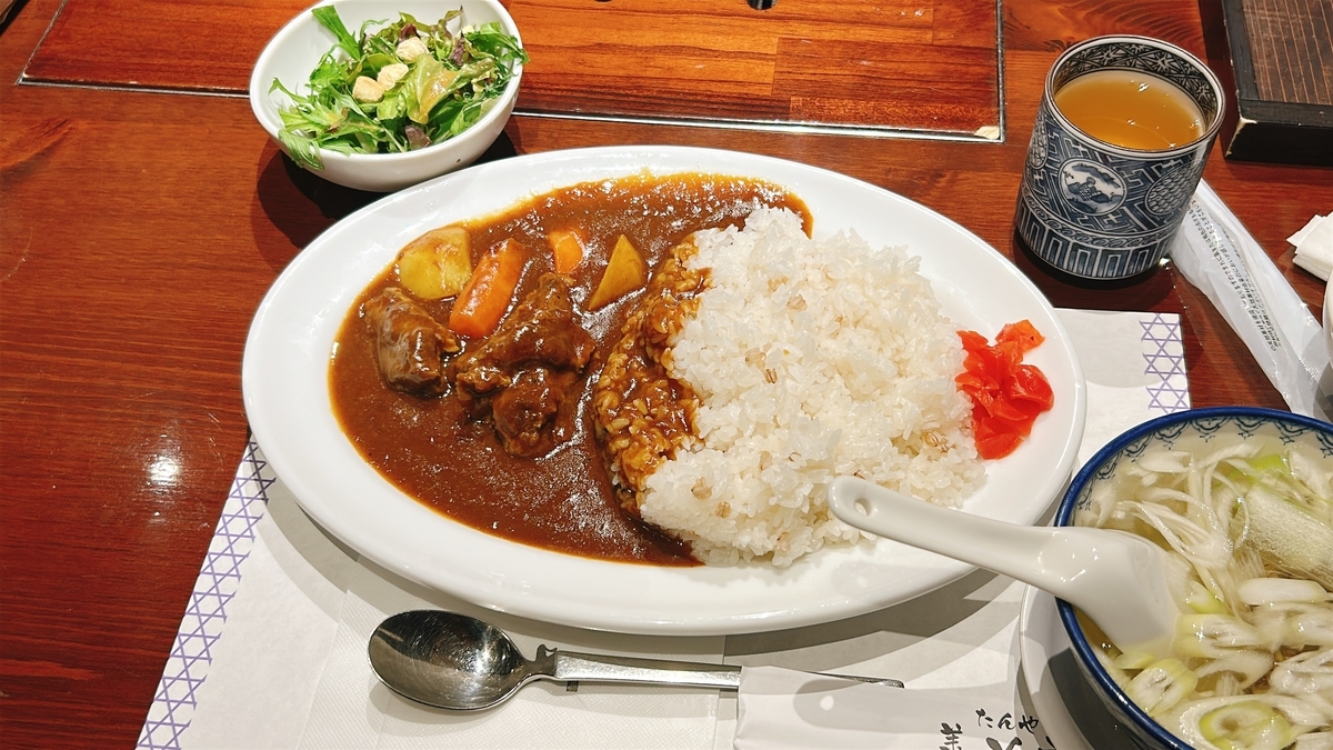 右手前にネギがたっぷり入った牛テールスープの器。その隣にカレーライスのお皿ががある。ごろっとしたお肉が主張している。