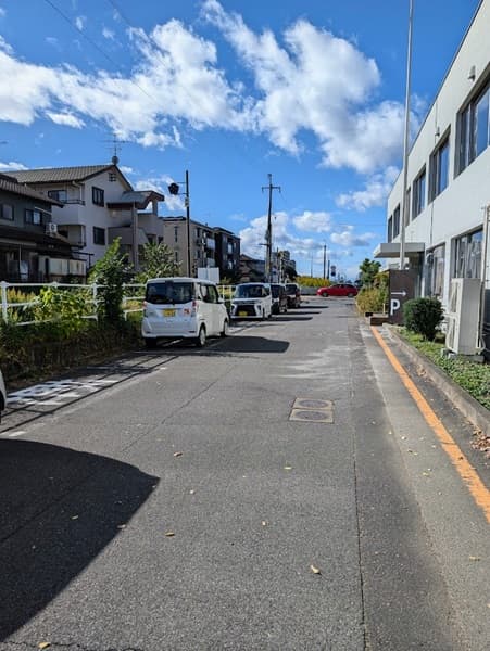 道の右に白いコンクリートの建物、左には車と線路