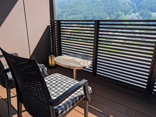 ベランダに小さな机と１脚の椅子、ベランダからは緑の山々
