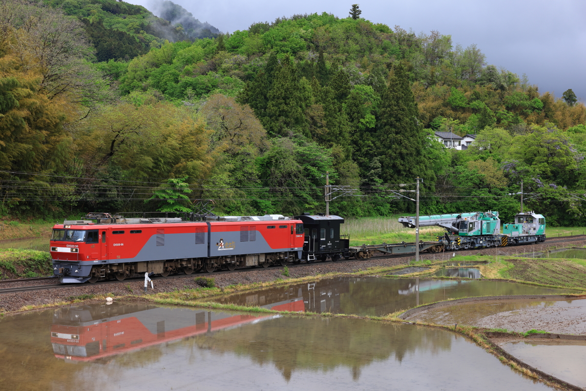 田植え直前の水田に姿を映す、EH500-56牽引の鉄道クレーン車KRC810Nを
