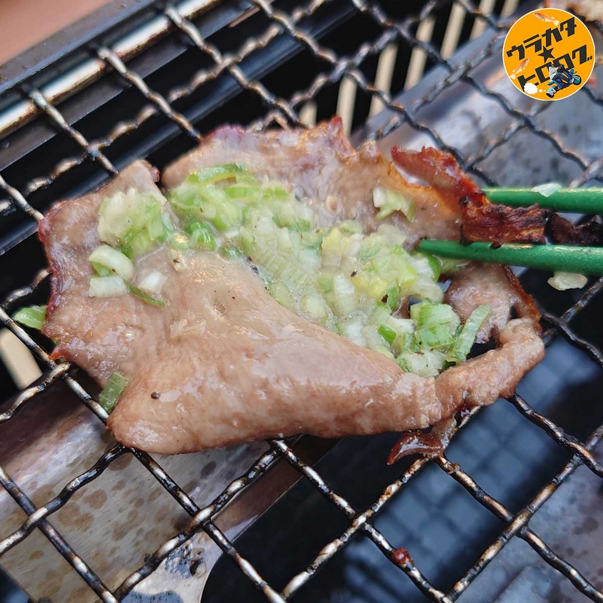 焼けた牛タンの上にネギ塩ダレをのせている様子