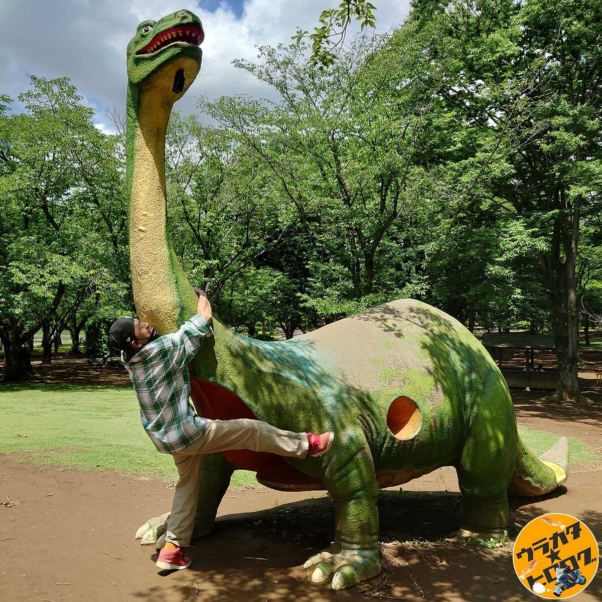 坂東市の八坂公園にある緑色で首が長い恐竜の首に絡みつく筆者(専属カメラマンによる撮影)
