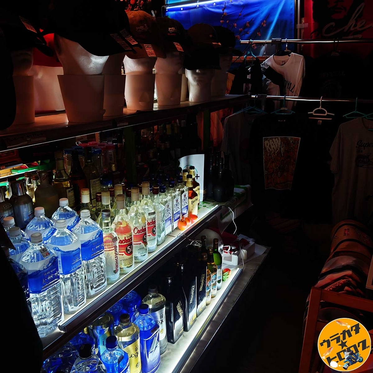 薄暗い店内で売られている酒と帽子とTシャツ(筆者撮影)