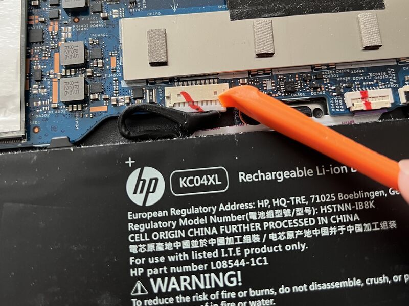 バッテリーのコネクタをヘラで少しずつ押し出して取り外している様子