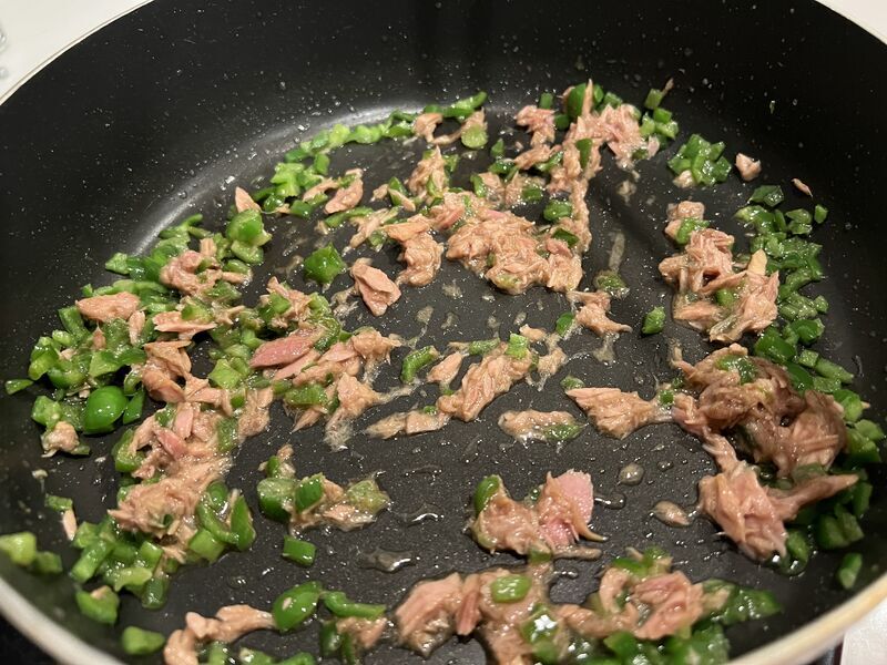 ツナの油で炒めたピーマンにツナと調味料を混ぜ合わせている様子
