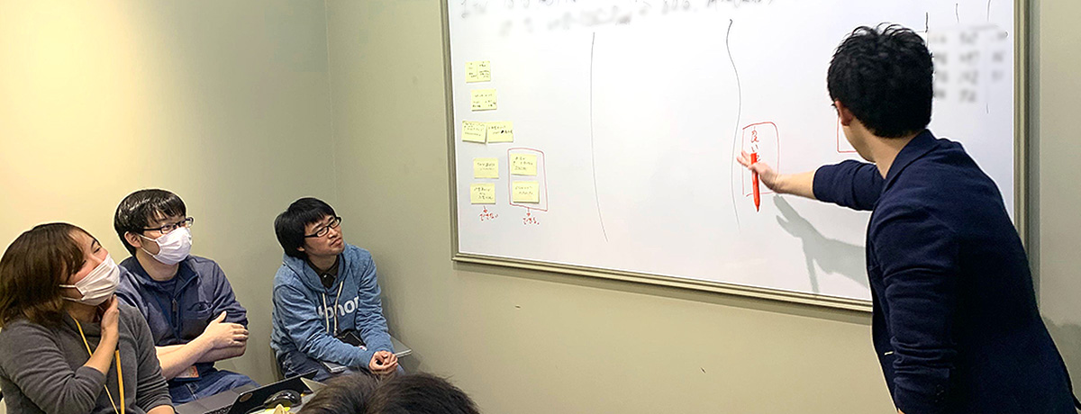 写真：ホワイトボードを書きながら説明する人と、聞き入る人