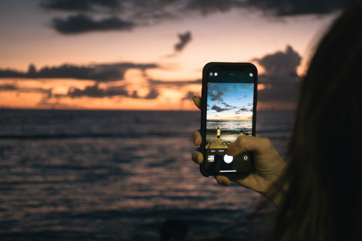 スマホで夕焼けと波打ち際を撮影するのフリー素材（写真）