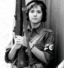 「チェ 28歳の革命」でアレイダ・マルチを演じているカタリーナ・サンディーノ・モレーノ、ドアの前で軍服で自動小銃を持った写真を白黒に変えてあるもの
