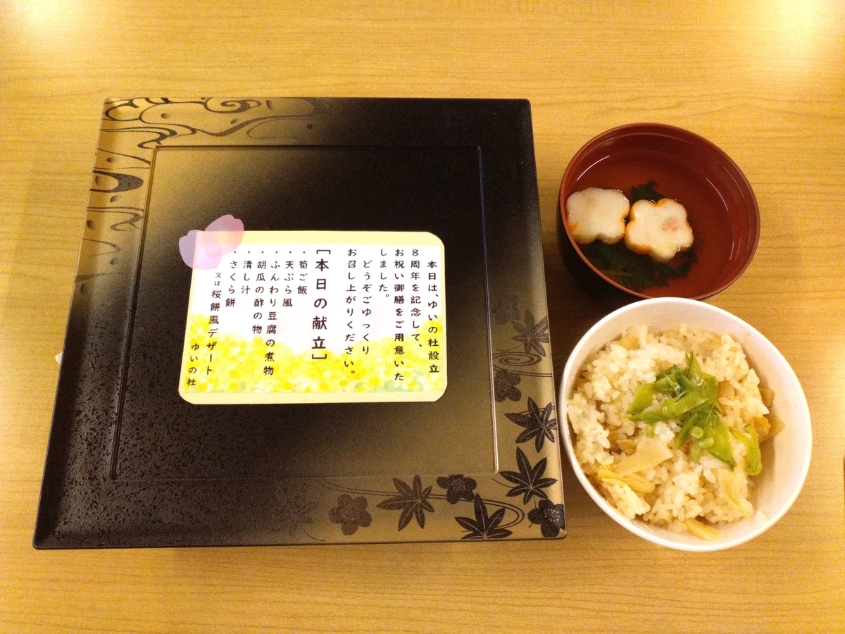 介護施設の食事風景。黒い器に日本語説明カードと共に、雑炊とみそ汁が配膳されている。