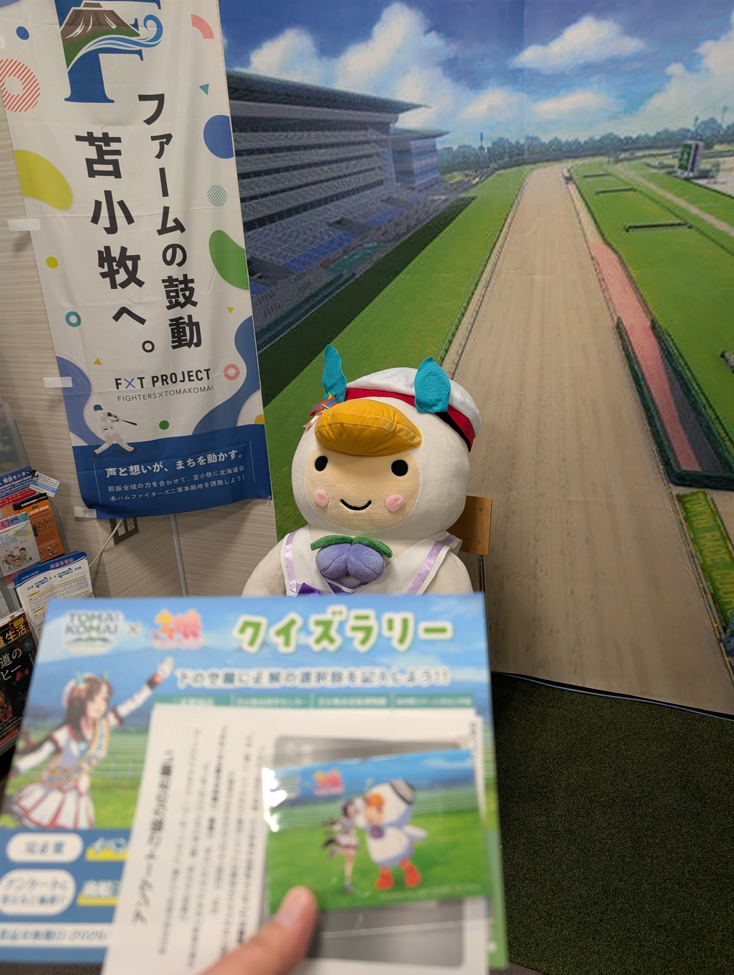 所内のパネルを背景に、クイズラリー台紙と完走賞カードを撮影。